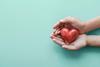 Two hands cupping a red wooden heart, shown from above