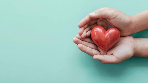 Two hands cupping a red wooden heart, shown from above