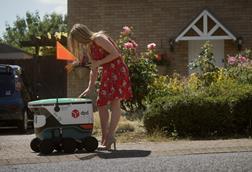 Woman receiving a delivery from a DPD robot outside a house