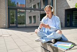 Student sitting outside on campus using smartphone