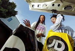 Two young people removing JD Sports carrier bags from a car boot