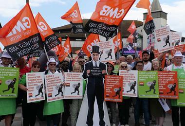 Asda workers on strike with flags and a cutout of TDR capital Manjit Dale